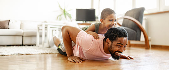 Father laughing as he does push-ups with son on his back